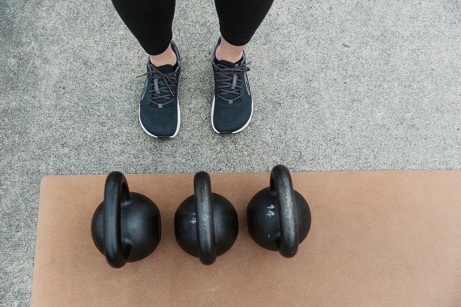 Three kettlebells on a yoga mat in front of a person standing, ready to work out.