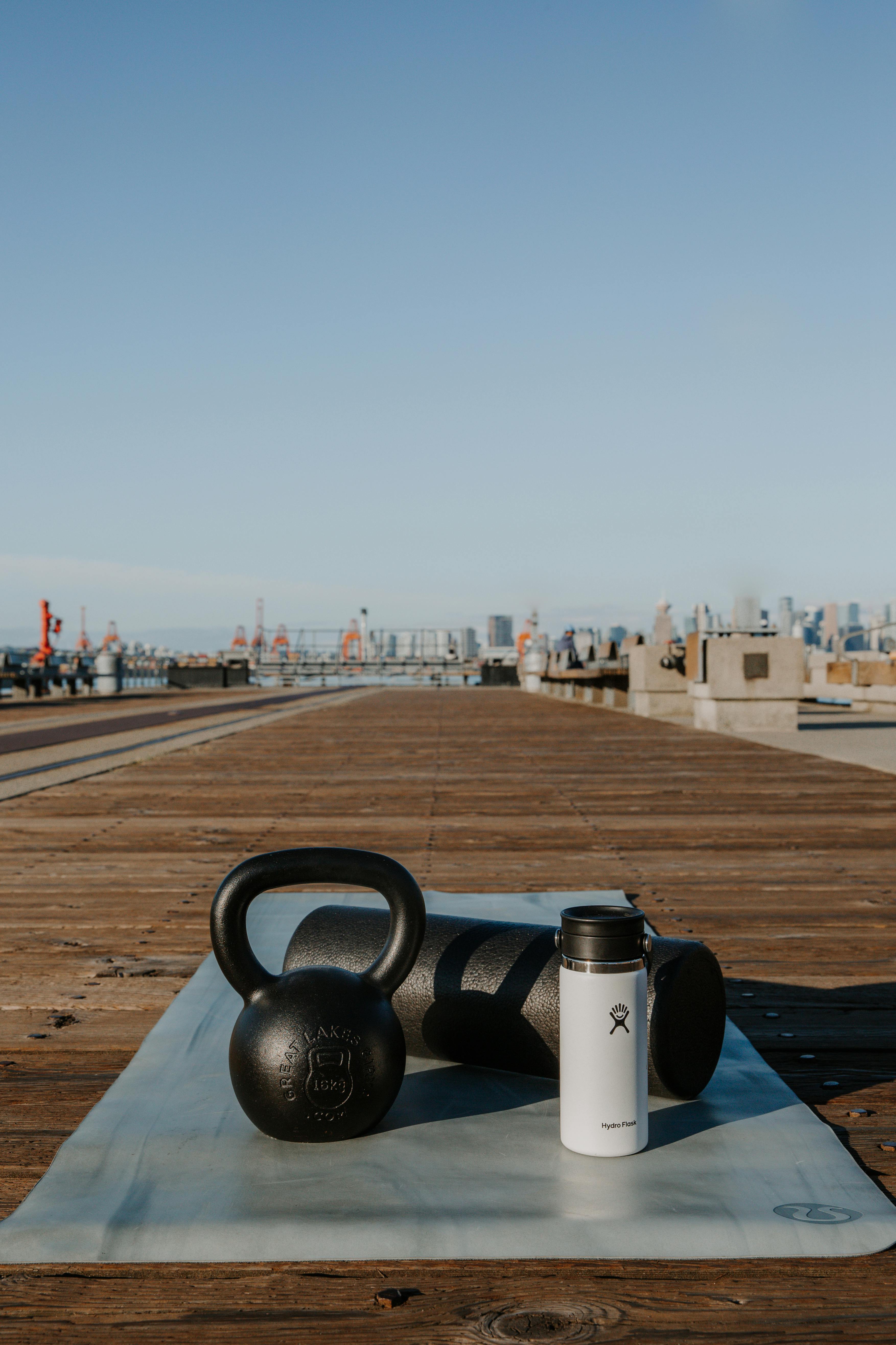 A kettlebell, water bottle, foam roller, and yoga mat on a dock